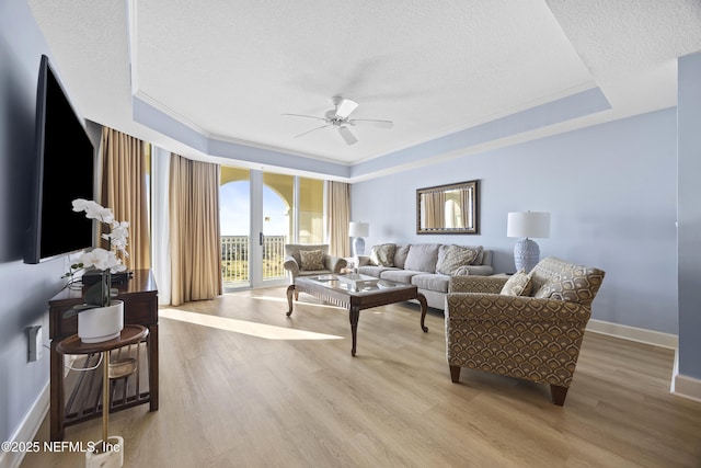 living room featuring a textured ceiling, ornamental molding, a tray ceiling, ceiling fan, and light hardwood / wood-style floors