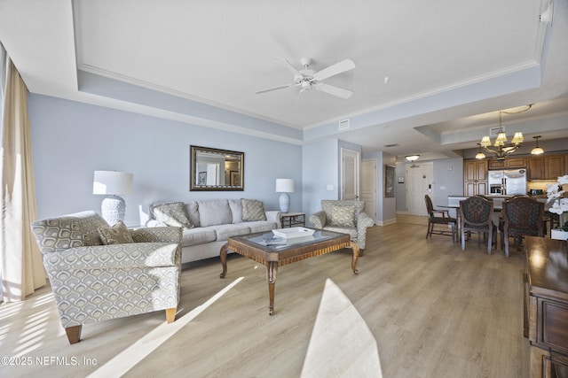 living room featuring ornamental molding, a tray ceiling, ceiling fan with notable chandelier, and light hardwood / wood-style flooring