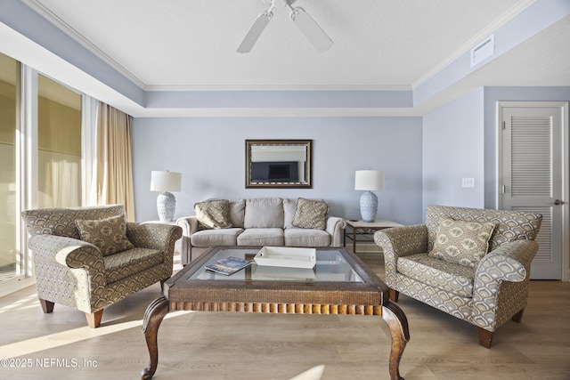 living room featuring ceiling fan, ornamental molding, a raised ceiling, and wood-type flooring