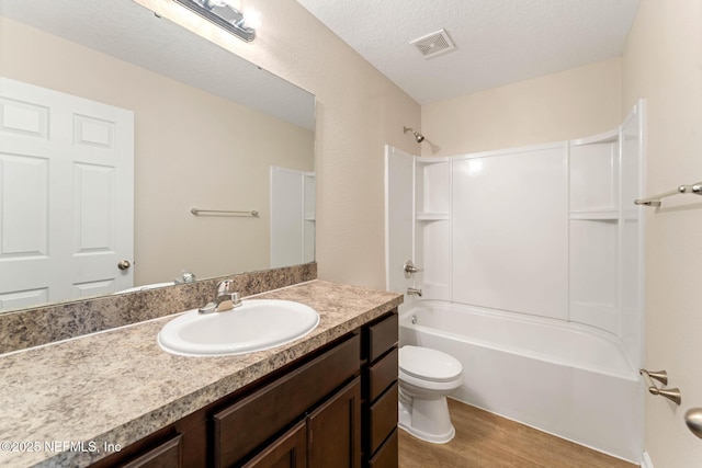 full bathroom with toilet,  shower combination, a textured ceiling, vanity, and hardwood / wood-style floors