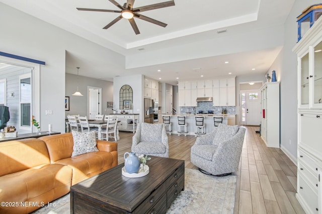 living room featuring ceiling fan, a raised ceiling, and light hardwood / wood-style floors