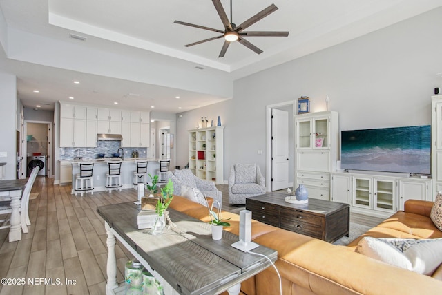 living room with ceiling fan, washer / dryer, light hardwood / wood-style floors, and a raised ceiling