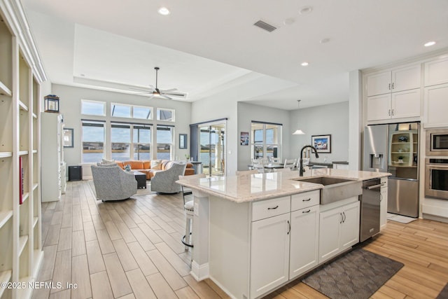 kitchen with sink, white cabinetry, stainless steel appliances, light stone countertops, and an island with sink