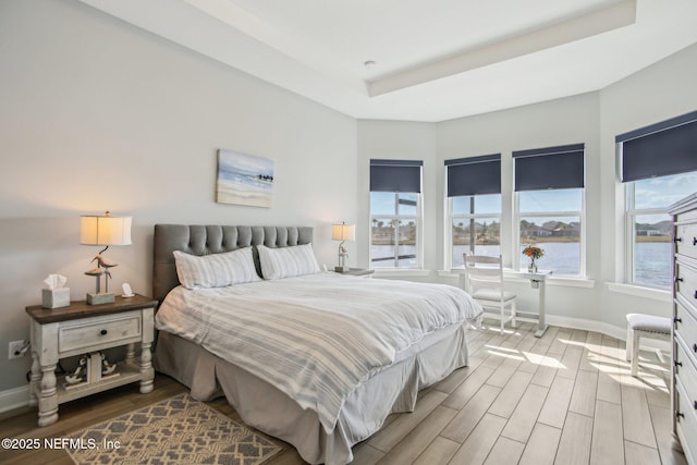 bedroom featuring a raised ceiling, a water view, and light hardwood / wood-style floors