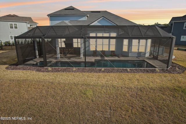 back house at dusk featuring a patio, a lanai, and a lawn