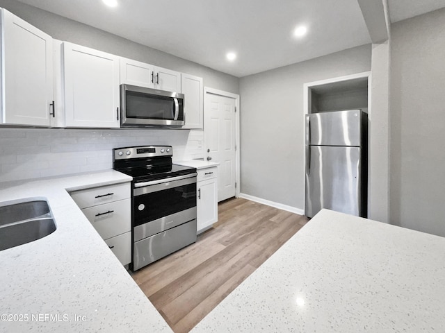 kitchen with tasteful backsplash, sink, white cabinets, light hardwood / wood-style floors, and stainless steel appliances