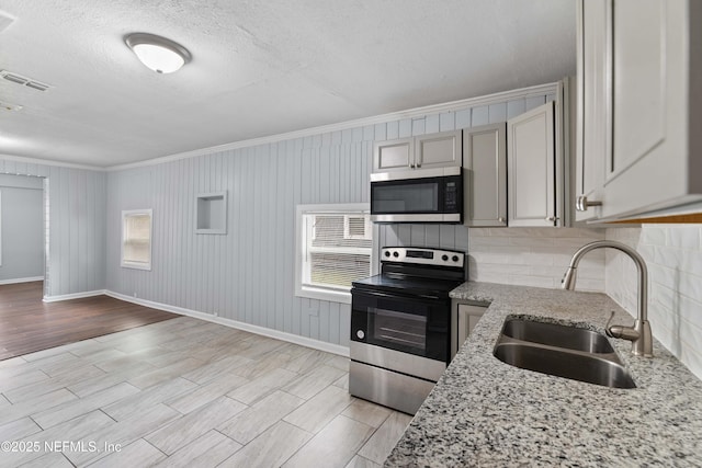 kitchen with sink, crown molding, stainless steel appliances, light stone counters, and a textured ceiling