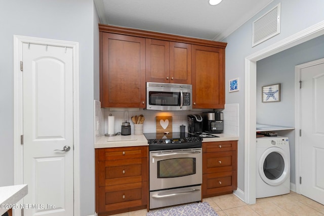 kitchen with appliances with stainless steel finishes, ornamental molding, decorative backsplash, light tile patterned flooring, and washer / dryer