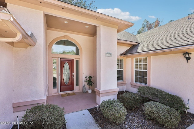 doorway to property featuring a shingled roof and stucco siding