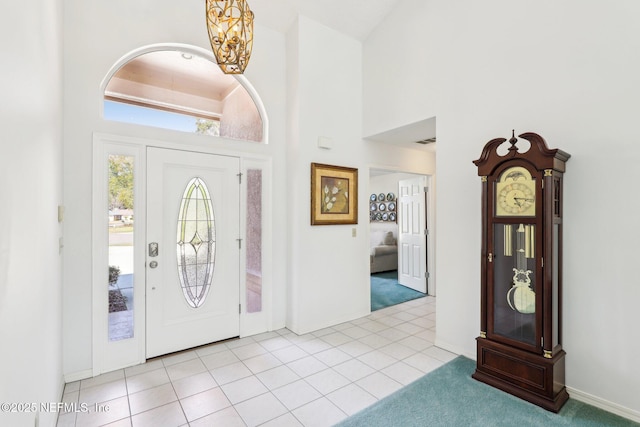 tiled entryway with a notable chandelier, a towering ceiling, visible vents, and baseboards