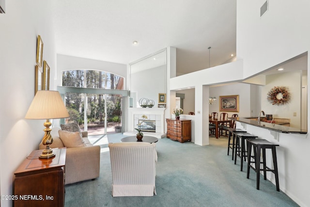 carpeted living area with a tile fireplace, visible vents, and a towering ceiling