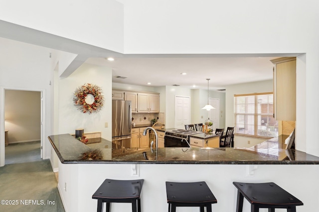 kitchen featuring stainless steel fridge, range, kitchen peninsula, decorative light fixtures, and cream cabinetry