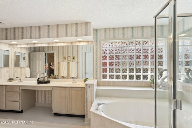 full bathroom featuring double vanity, wallpapered walls, a textured ceiling, and a sink