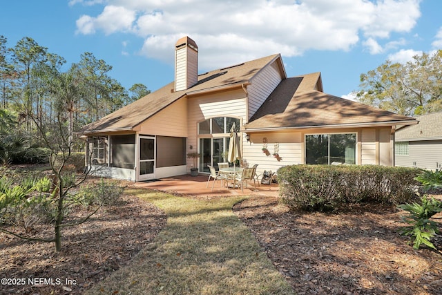 back of property featuring a chimney, a patio area, and a sunroom