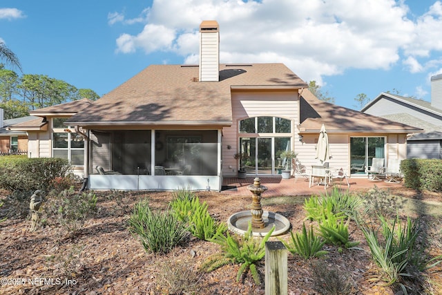 rear view of house with a sunroom, a shingled roof, and a chimney