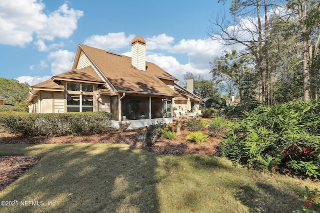 rear view of house featuring a lawn, a chimney, and a sunroom