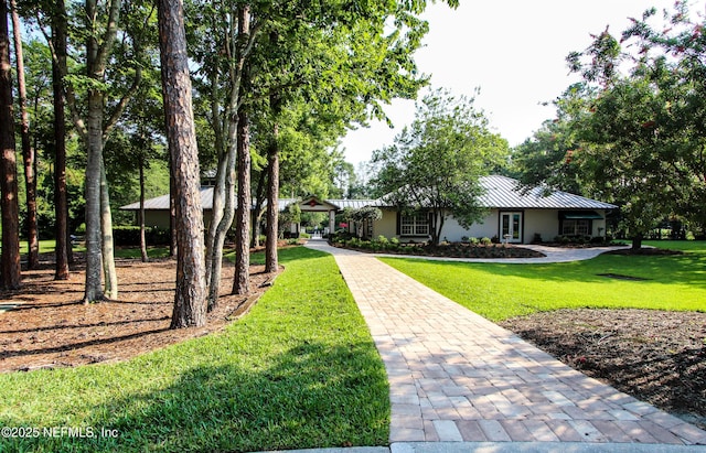 ranch-style home featuring metal roof, a standing seam roof, a front yard, and stucco siding