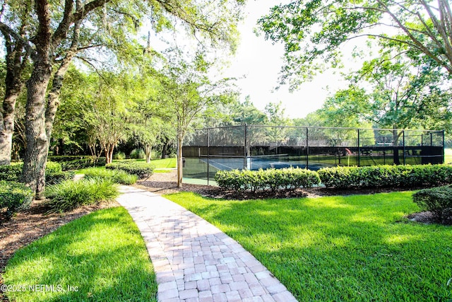 surrounding community featuring a tennis court, fence, and a yard