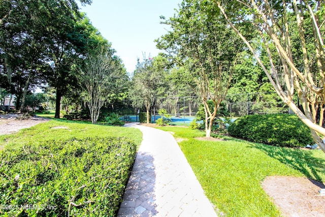 view of property's community with a tennis court, a lawn, and fence