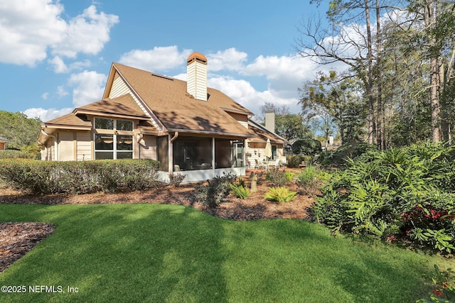 back of house with a sunroom, a chimney, and a lawn