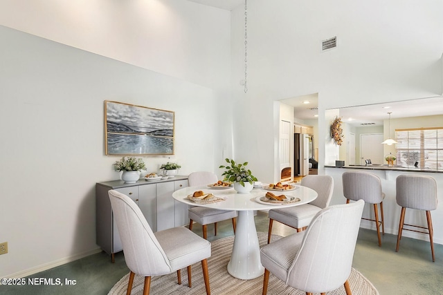 dining room featuring a high ceiling, light colored carpet, visible vents, and baseboards