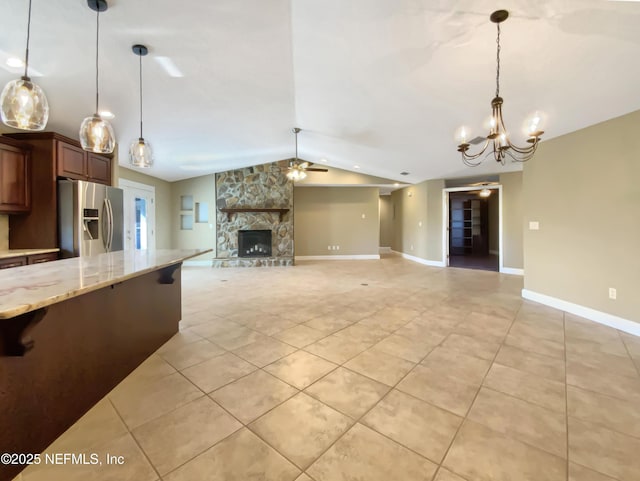 kitchen with lofted ceiling, hanging light fixtures, light stone counters, stainless steel fridge with ice dispenser, and ceiling fan with notable chandelier