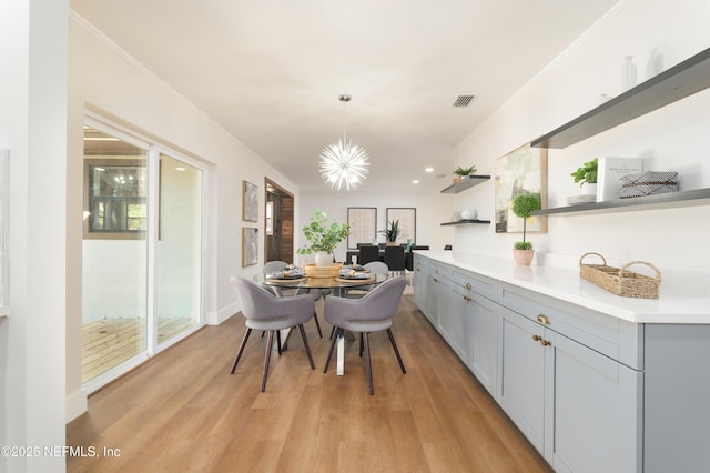 dining room with an inviting chandelier, ornamental molding, and light hardwood / wood-style flooring