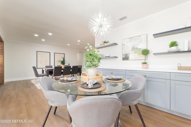 dining area with ornamental molding, a chandelier, and light hardwood / wood-style floors