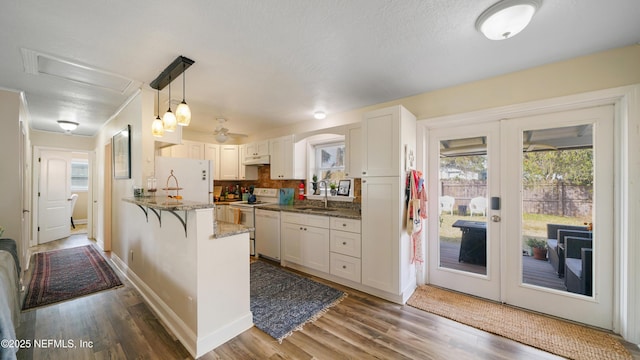 kitchen with white appliances, kitchen peninsula, sink, and white cabinets