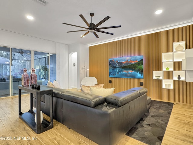 living room with wood-type flooring, crown molding, wooden walls, and ceiling fan