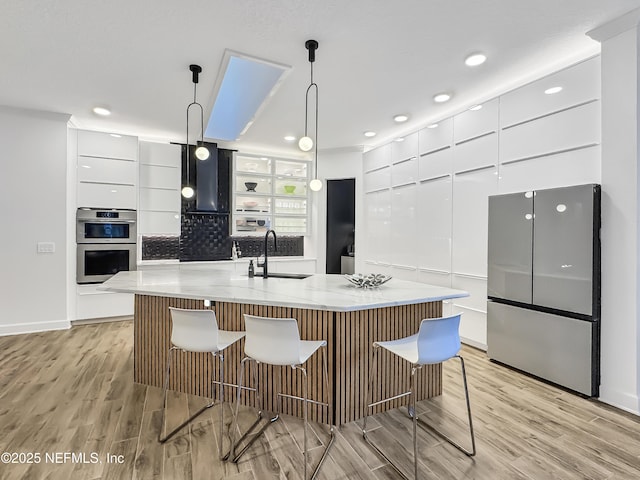 kitchen featuring appliances with stainless steel finishes, white cabinetry, sink, hanging light fixtures, and a large island with sink