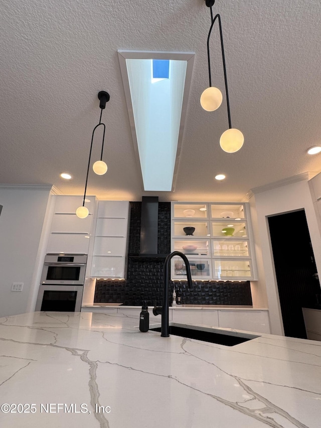 kitchen featuring sink, white cabinetry, hanging light fixtures, double oven, and light stone countertops