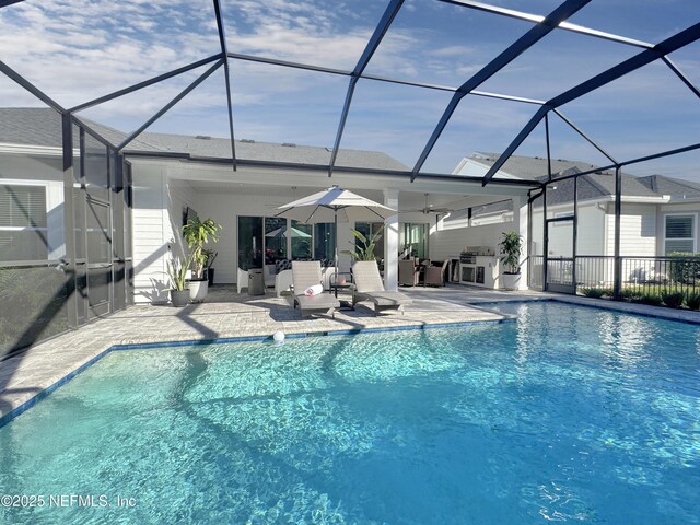 view of pool with ceiling fan, an outdoor kitchen, glass enclosure, and a patio area