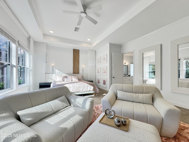 carpeted bedroom with a tray ceiling, ensuite bath, and ceiling fan