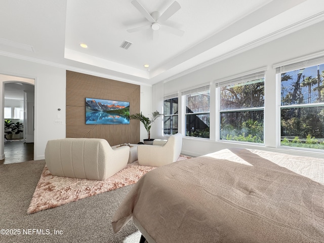 bedroom with multiple windows, ornamental molding, ceiling fan, and a tray ceiling