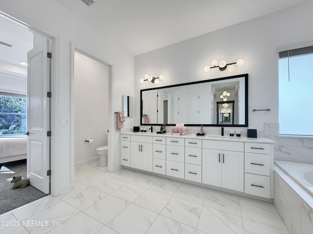 bathroom featuring toilet, a healthy amount of sunlight, vanity, and tiled bath