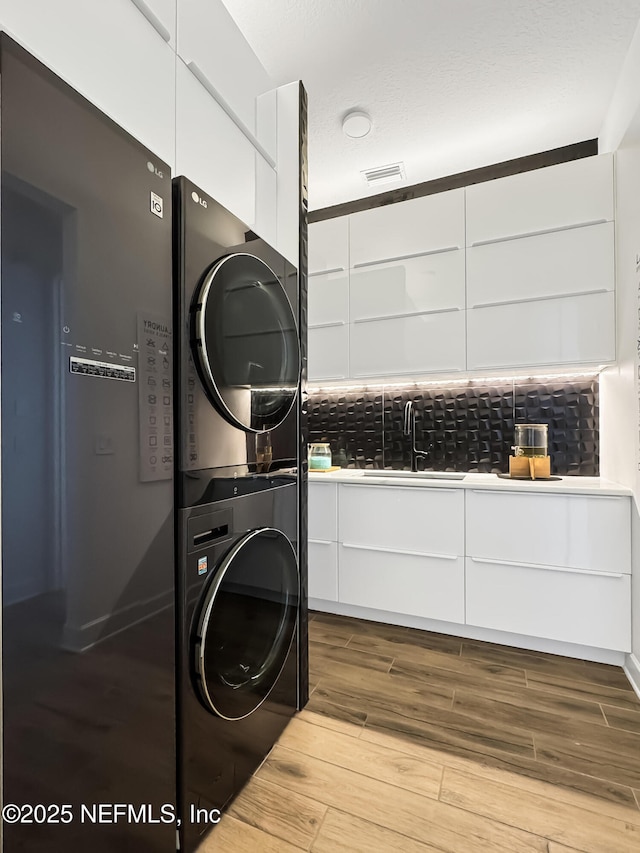 laundry room featuring stacked washer / drying machine, sink, and light wood-type flooring