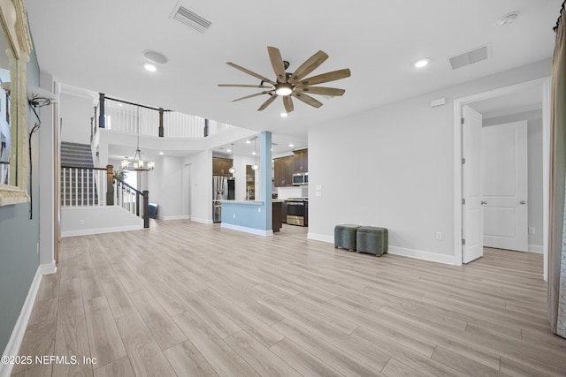 unfurnished living room featuring ceiling fan with notable chandelier and light wood-type flooring