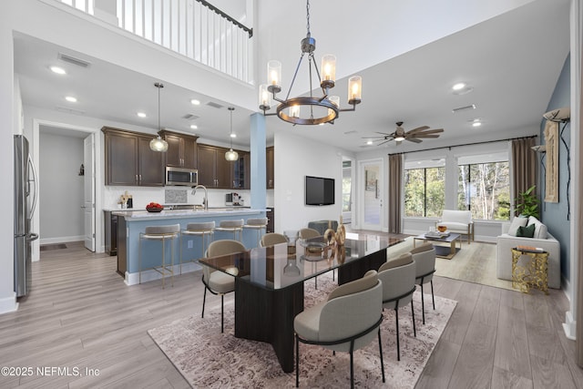 dining space featuring a high ceiling, sink, ceiling fan with notable chandelier, and light hardwood / wood-style flooring