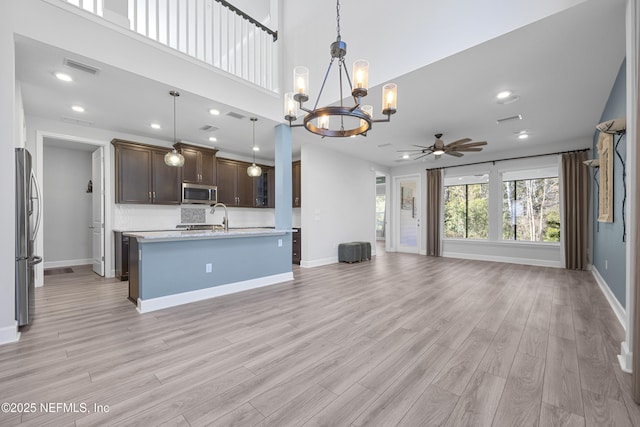 kitchen with dark brown cabinets, hanging light fixtures, appliances with stainless steel finishes, an island with sink, and light hardwood / wood-style floors