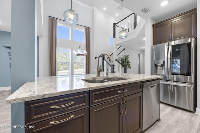 kitchen with appliances with stainless steel finishes, sink, light hardwood / wood-style floors, light stone countertops, and a center island with sink