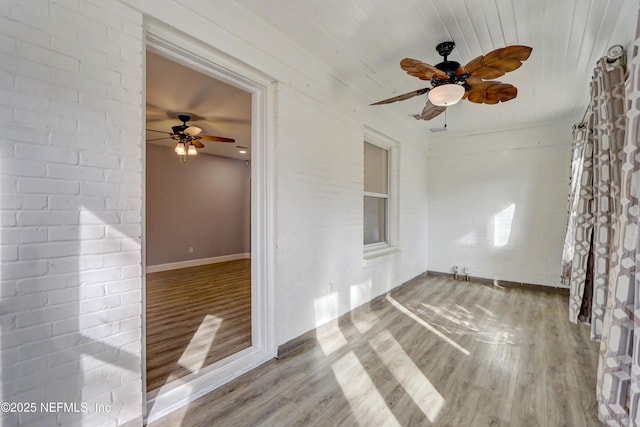 empty room featuring hardwood / wood-style floors, ceiling fan, and brick wall