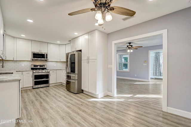 kitchen with sink, light hardwood / wood-style flooring, appliances with stainless steel finishes, decorative backsplash, and white cabinets