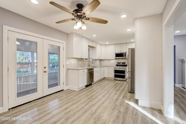 kitchen featuring appliances with stainless steel finishes, white cabinetry, decorative backsplash, light wood-type flooring, and french doors