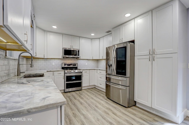 kitchen with stainless steel appliances, light stone countertops, sink, and white cabinets