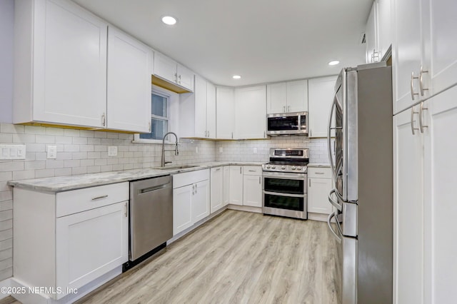 kitchen with sink, white cabinetry, light hardwood / wood-style flooring, appliances with stainless steel finishes, and light stone countertops