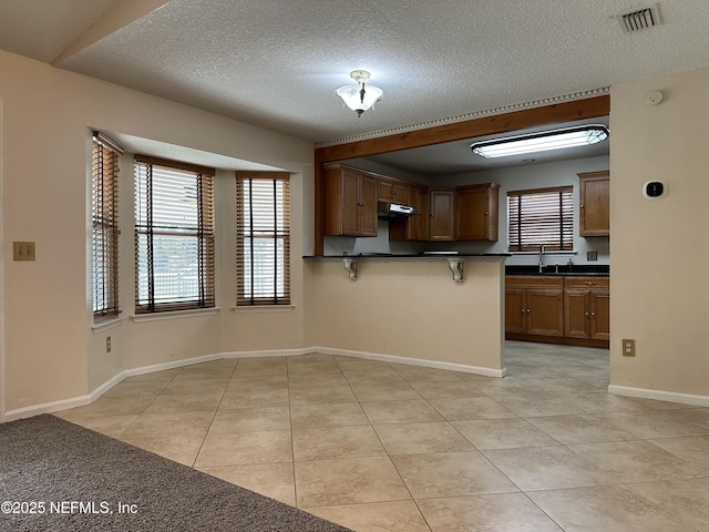 kitchen with sink, a breakfast bar, a textured ceiling, light tile patterned flooring, and kitchen peninsula