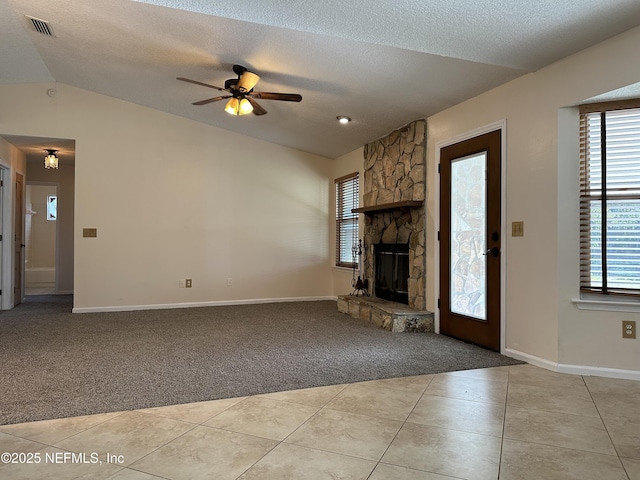 unfurnished living room featuring light tile patterned flooring, vaulted ceiling, a stone fireplace, and a textured ceiling