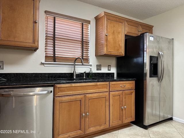 kitchen with sink, light tile patterned floors, dark stone countertops, stainless steel appliances, and a textured ceiling