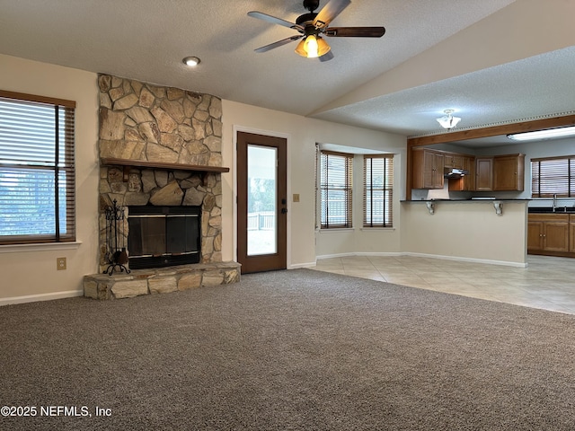 unfurnished living room with a stone fireplace, light colored carpet, a healthy amount of sunlight, and a textured ceiling